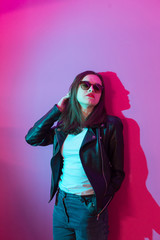 Fashioned girl in leather jacket in dark glasses in pink anf blue  neon lights background. 