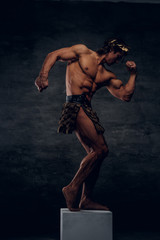 Fototapeta na wymiar Attractive young bodybuilder is posing on pedestal. He is wearing wreath and bandage.