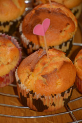 close up view of homemade sweet and golden baked muffins, homemade muffins with cracks on cooling metal grid on wooden table with love decoration