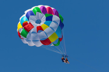 With a parachute for parasailing a couple flies through the air with blue sky in the background.