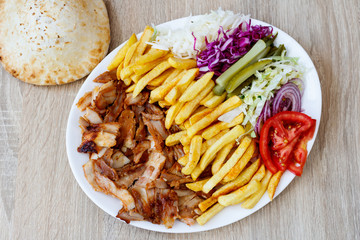 Chiken Doner Kebab on the plate with bread, french fries, tomatoes, onion, pickles and salad on a...
