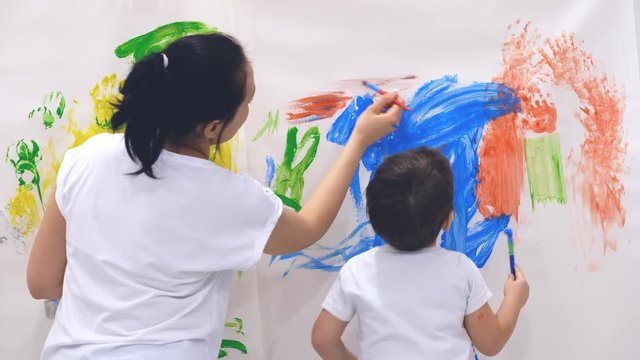 Close up of happy little child making colorful handsprint on the white wall with mother together. Slow motion