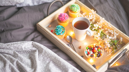 Morning breakfast in bed. Wooden tray with coffee or tea and cupcakes. Gray bedspread in the interior of a hotel room. Copy space