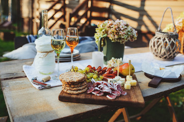 wine, cheese, ham and fruits served on wooden cutting board. Summer outdoor garden party