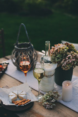 evening summer garden party with wine, cheese and fruits on wooden table decorated with candles and flowers