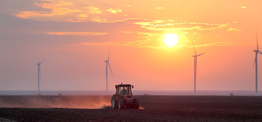 Tractor in field and windmillsin sunrise or sunset