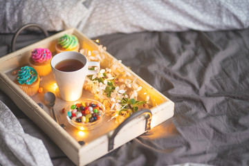 Morning breakfast in bed. Wooden tray with coffee or tea with bright cakes. Gray cover of the hotel room interior. Copy space, flat lay