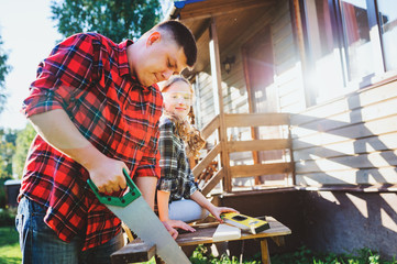 father teaching kid daughter to use tools. Girl helping dad with building work outdoor in summer,...