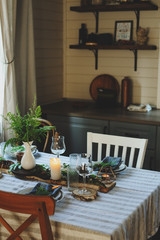 rustic country kitchen interior with festive table setting for summer dinner in natural green and brown tones. Small wooden cottage.