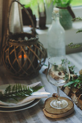rustic festive table details with wild ferns, handmade decoration and candles. Country home dinner in summer evening.