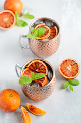 Blood orange Moscow mule alcohol cocktail with fresh mint leaves and ice in copper mugs on a gray...