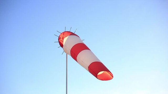 Striped red and white wind vane against a clear blue sky.
