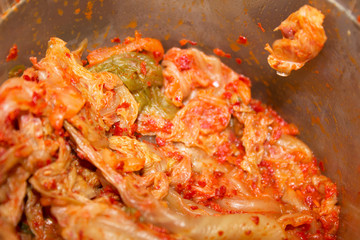 Close-up of red spicy Korean fermented napa cabbage radish kimchi in a plastic jar