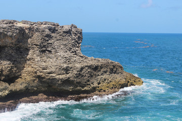 Teal ocean water with white sea foam crashing and old rock island Barbados
