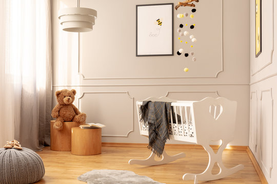 Teddy bear on wooden stool in fashionable nursery with white wooden cradle with grey blanket