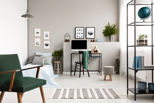 Green vintage armchair in stylish forest inspired teenager's bedroom and workspace, copy space on empty wall