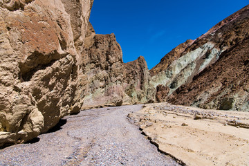 Fototapeta premium A dry riverbed of rocks and gravel curves through a canyon with colorful cliffs - Gower Gulch in Death Valley National Park