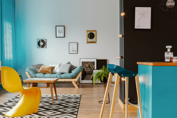 Open space loft interior with blue curtains, lounge with cushions, many posters and black wall by the home bar in real photo