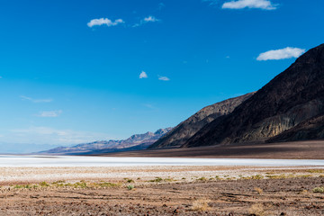 A vast barren desert landscape of salt flats with a mountain range receding into the distance under a blue sky with puffy white clouds - Death Valley National Park