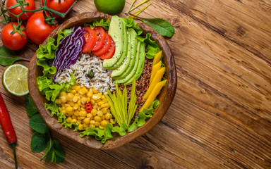 Buddha bowl with chickpea, avocado, wild rice, quinoa seeds, bell pepper, tomatoes, greens, cabbage, lettuce on old wooden table. Top view with copy space. Healthy vegan food.