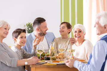 Smiling boy sitting between father and mother during family dinner with grandmother