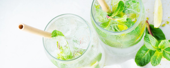 Flat lay of two glasses with tropical mojito cocktail on light background. Long wide banner with...