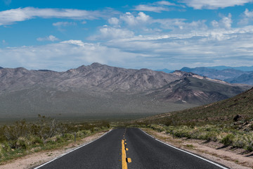 A highway moving towards perspective toward a mountain range in the desert landscape of Death Valley National Park
