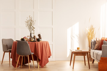 Dry flowers in vase on dining table covered with dark orange tablecloth