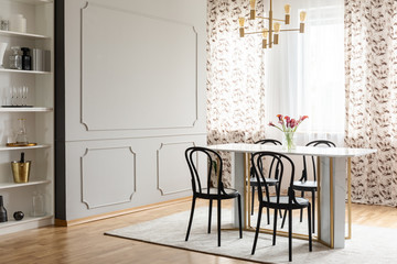 Fancy dining room interior with molding on a gray wall and elegant black chairs around a marble and golden table