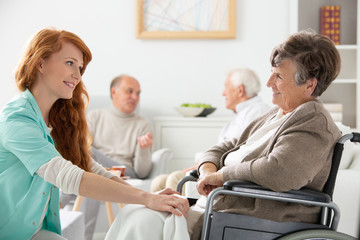 Obraz premium Happy caregiver supporting paralysed smiling elderly woman in the wheelchair