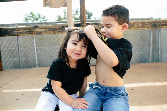 Brother lifts his shirt and places it on little sister's head