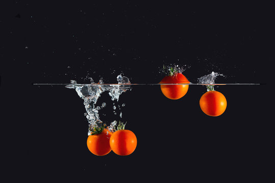Cherry tomatoes dipped in water splash on black background
