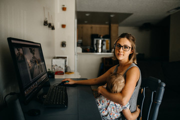 Working mother on computer holding baby and looking at camera