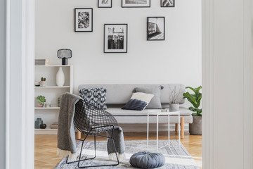Fancy black metal chair with grey blanket next to grey pouf in trendy living room
