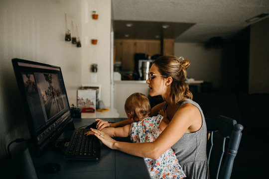 Multitasking working mother holding baby and typing on computer