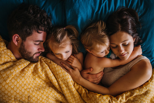 Family of four cuddling in bed