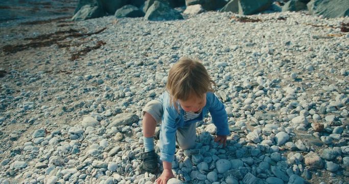 Little toddler picking up two big stones on the beach