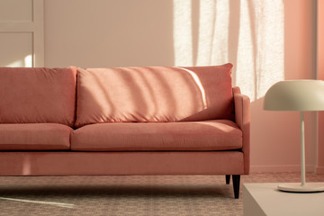 Pastel pink couch in white living room interior, copy space on empty wall
