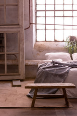 Wooden bench next to bed with grey blanket in simple bedroom interior with window. Real photo