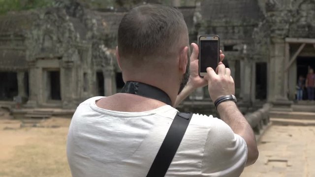 Man using smartphone and camera while doing photos of old ruins 