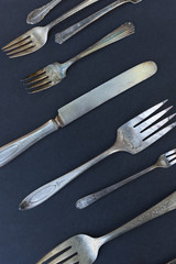 Weathered silverware of multiple sizes and patterns are arranged against a black background