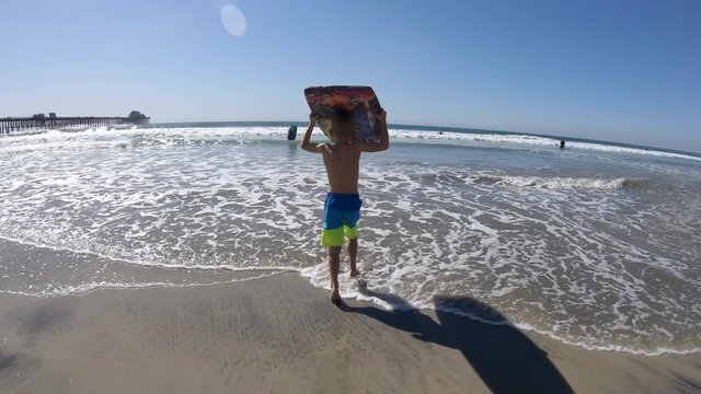 Boy Running into Ocean With Boogie Board