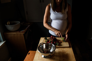 expectant mother chopping strawberries in the kitchen in low light