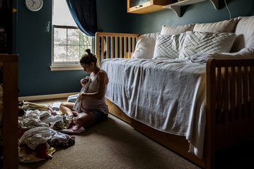 expectant mother sitting on nursery floor folding baby clothing