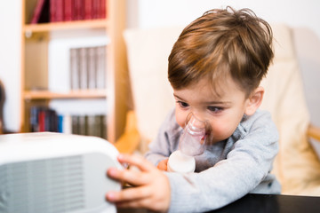 Little boy using steam inhaler nebulizer mask inhalation at home. Medical procedures vapor...