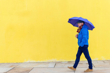 Confident senior man holding an umbrella walking against yellow wall
