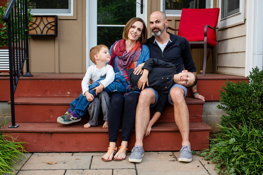 A Happy Family Sit Close Together On Their Front Stoop