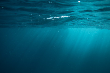 An underwater view of sun rays penetrating surface of blue ocean
