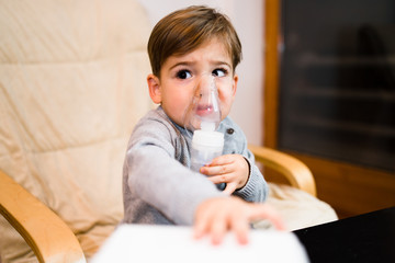 Little boy using steam inhaler nebulizer mask inhalation at home. Medical procedures vapor...