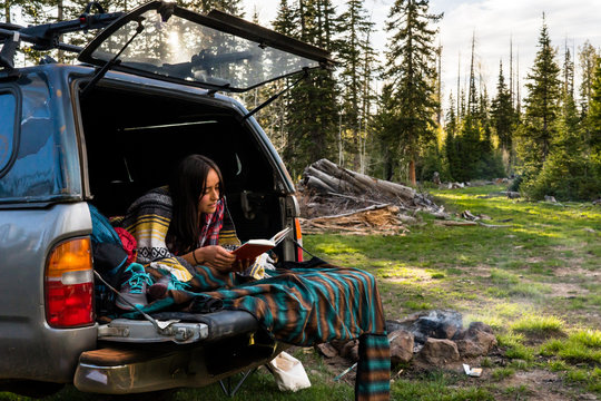 Camp Reads - Young woman reading while car camping in forest